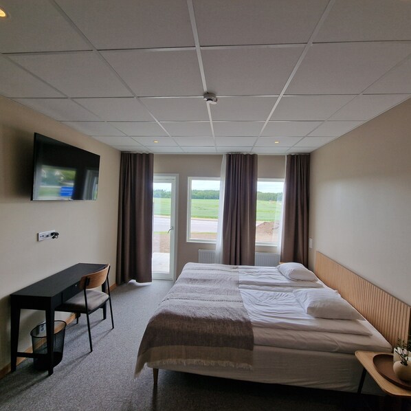 Habitación de hotel con cama, escritorio, silla, televisión y vistas al exterior.
