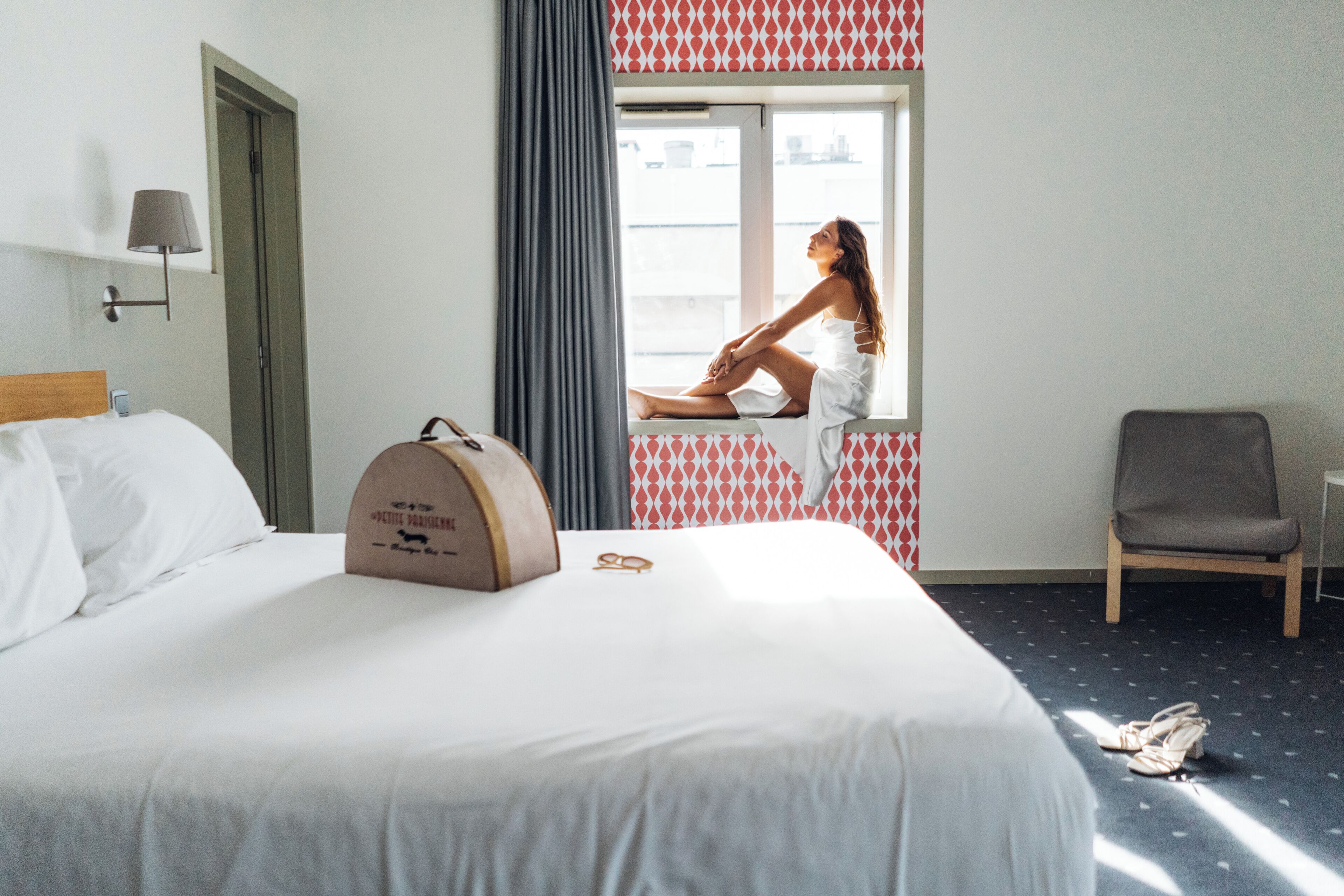 Une chambre d’hôtel avec un lit, une valise, une chaise et une fenêtre donnant sur un paysage agréable.
