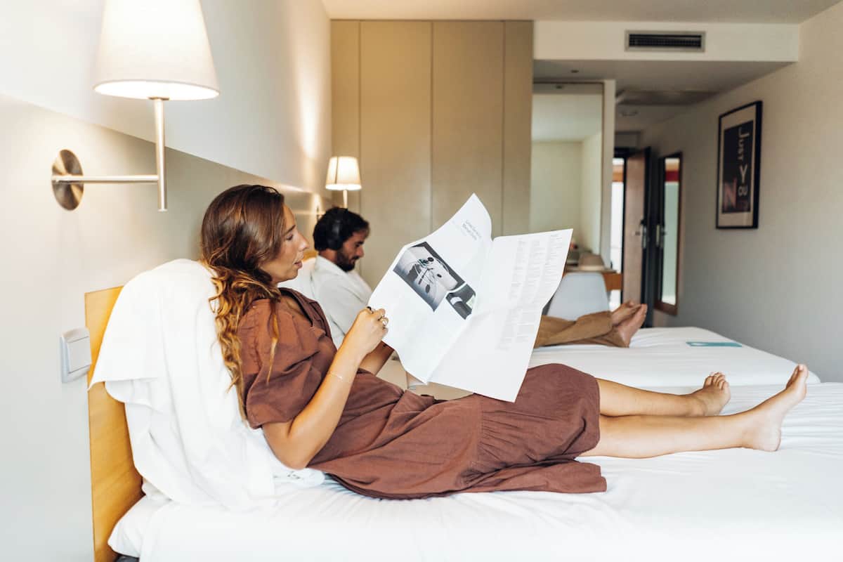 A hotel room with a bed, a reading lamp, and a wall-mounted light fixture.