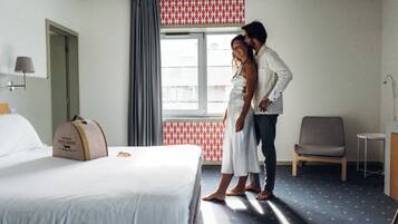 A hotel room with a bed, a suitcase, a chair, and a window with curtains.