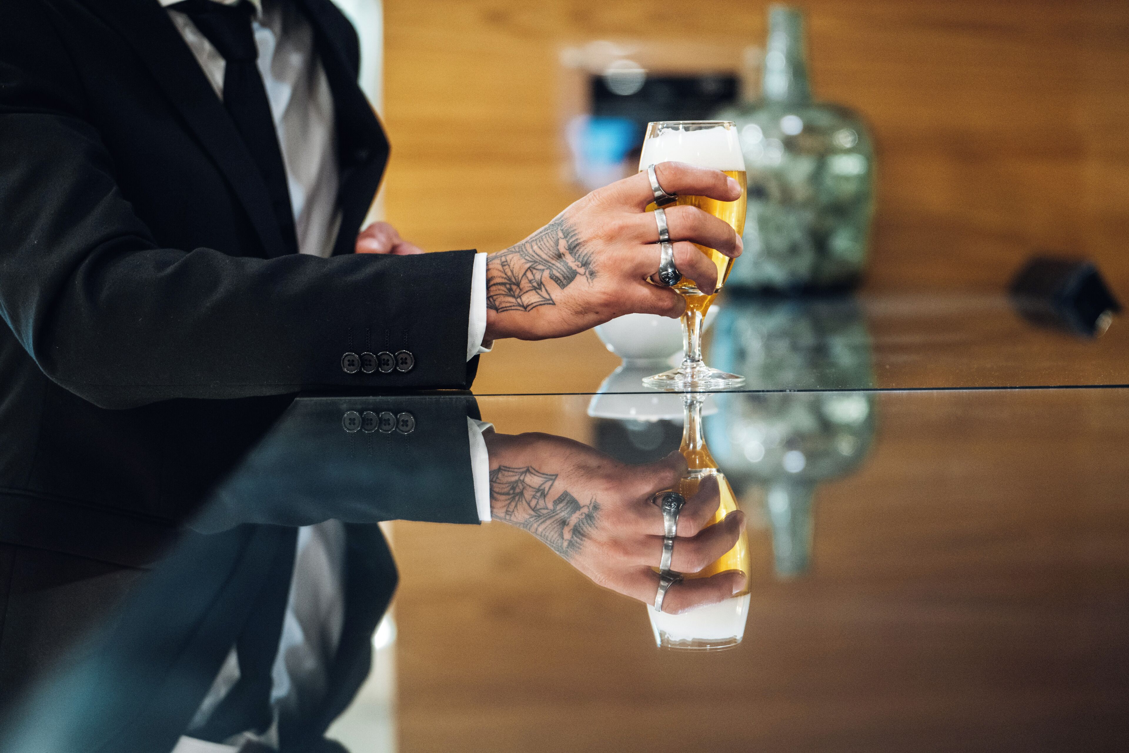 Uma pessoa vestida com terno segurando uma cerveja, com uma mão tatuada à mostra.