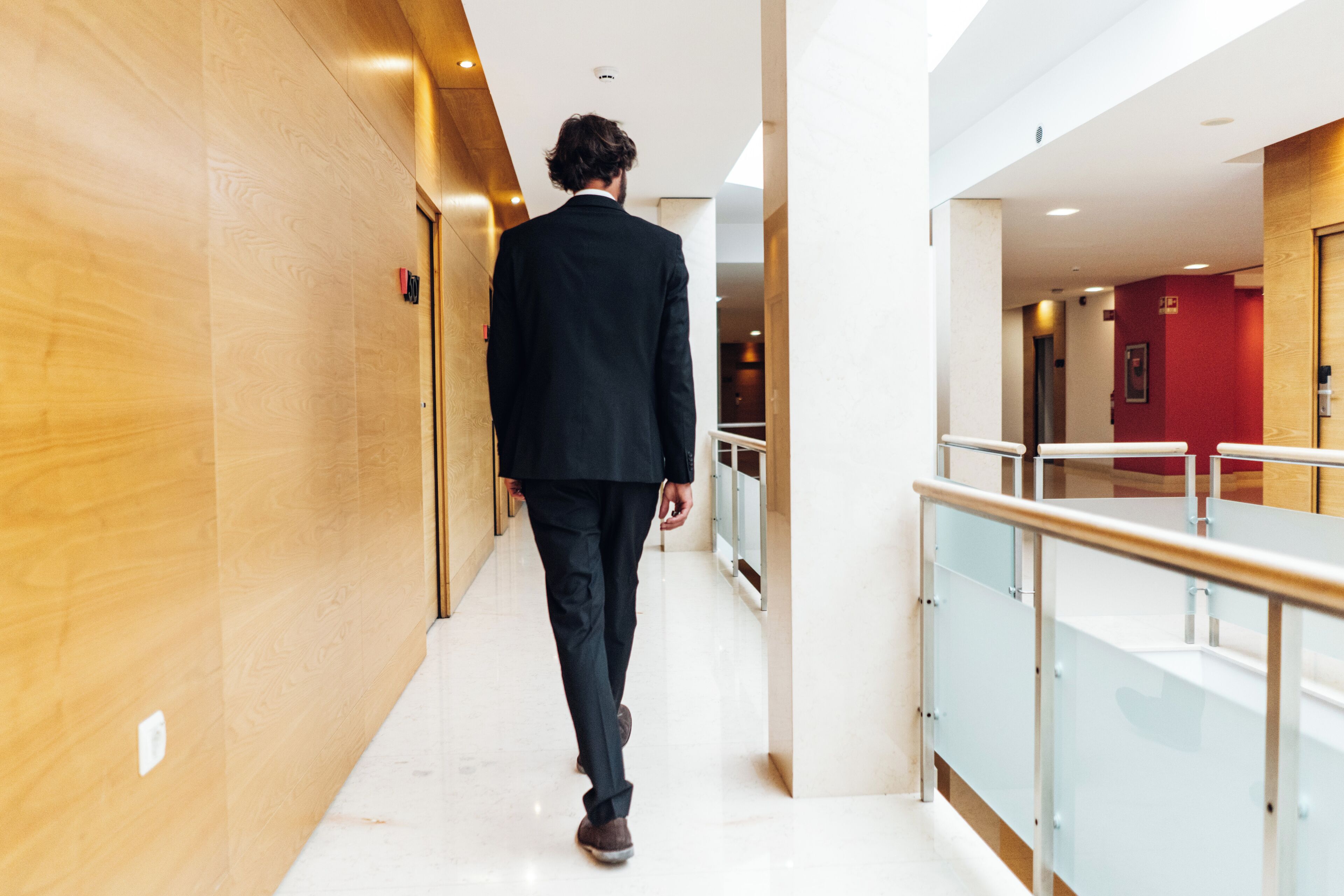 A man walking down a corridor with wooden walls and a glass railing.