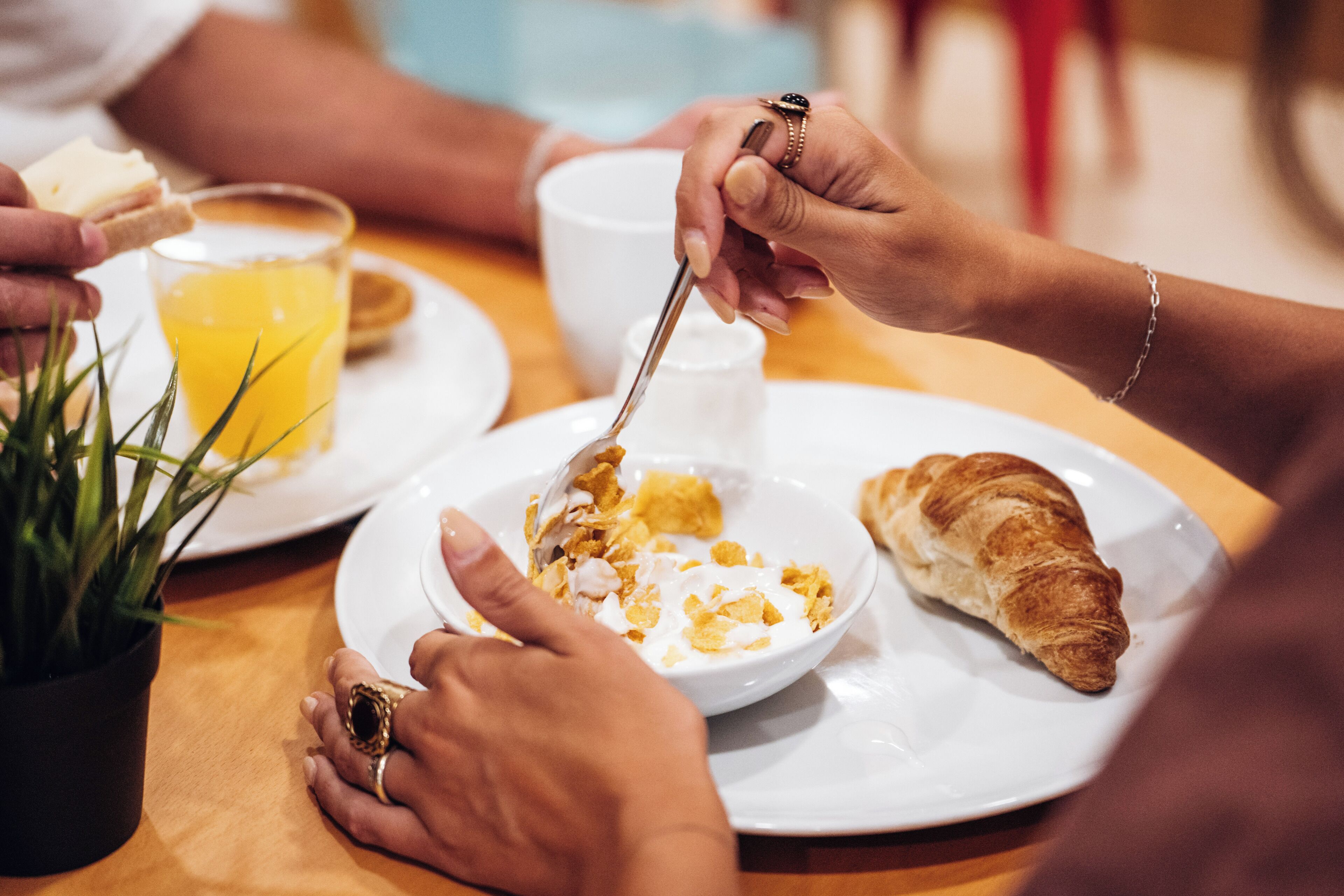 A dining table with a plate of cereal, a croissant, and a glass of orange juice.