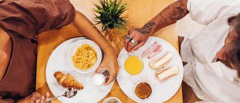 Un desayuno con platos de comida, una taza de café y una pequeña planta sobre una mesa de madera.