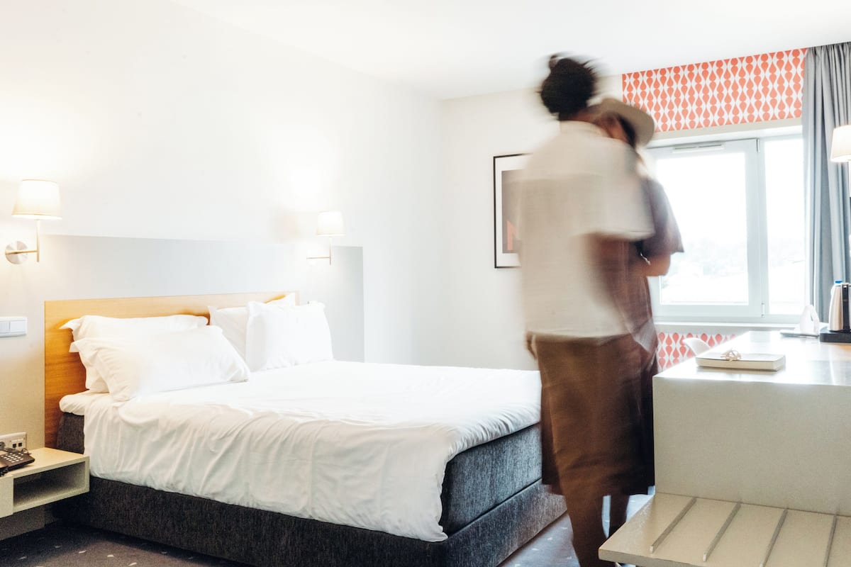 A hotel room with a bed, bedside table, lamp, and a window with curtains.
