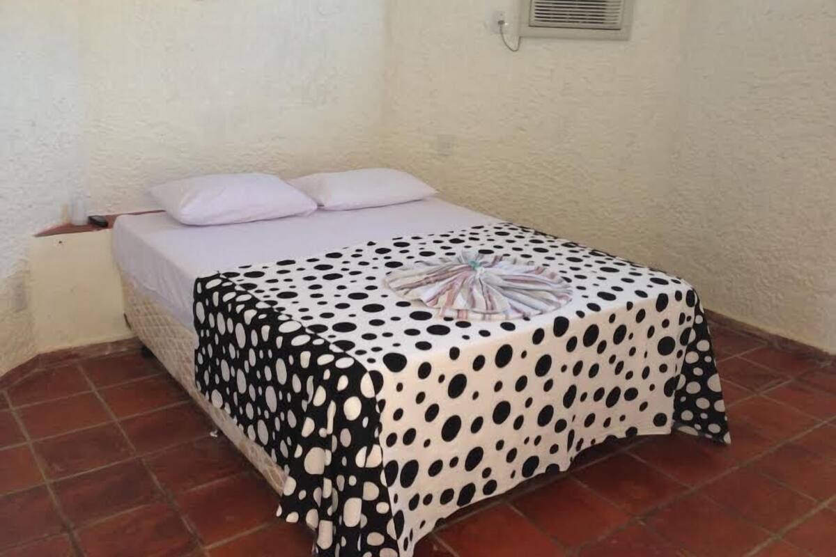 A bedroom with a bed, white walls, a polka dot bedspread, and a tiled floor.