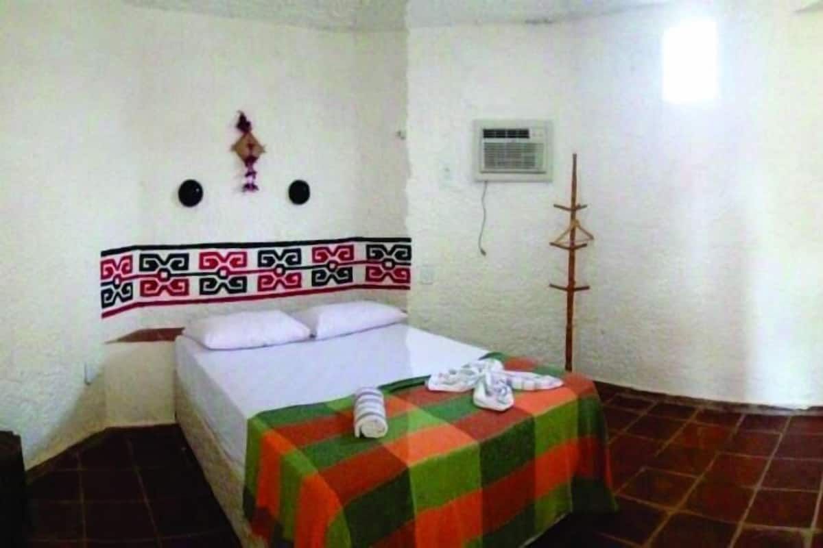 A small, simple room with a bed, a TV, and a refrigerator.