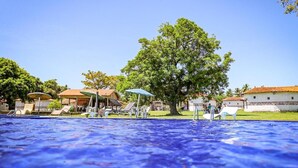 A swimming pool with lounge chairs and umbrellas, surrounded by buildings and trees. - Pousada Marajoara (Soure)