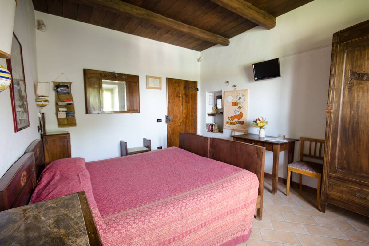 A bedroom with a large bed, wooden furniture, a desk, a chair, a television, and a wardrobe.