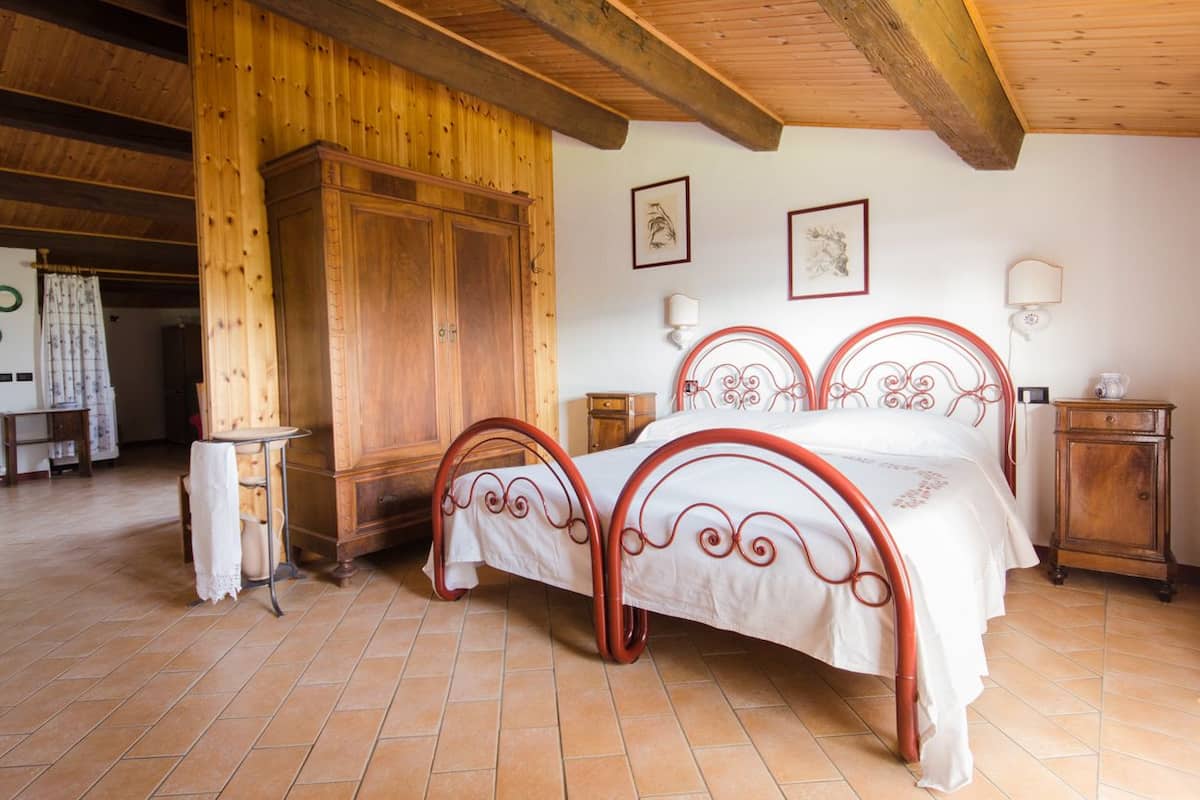 A bedroom with a wooden wardrobe, a bed with a red metal frame, and a tiled floor.