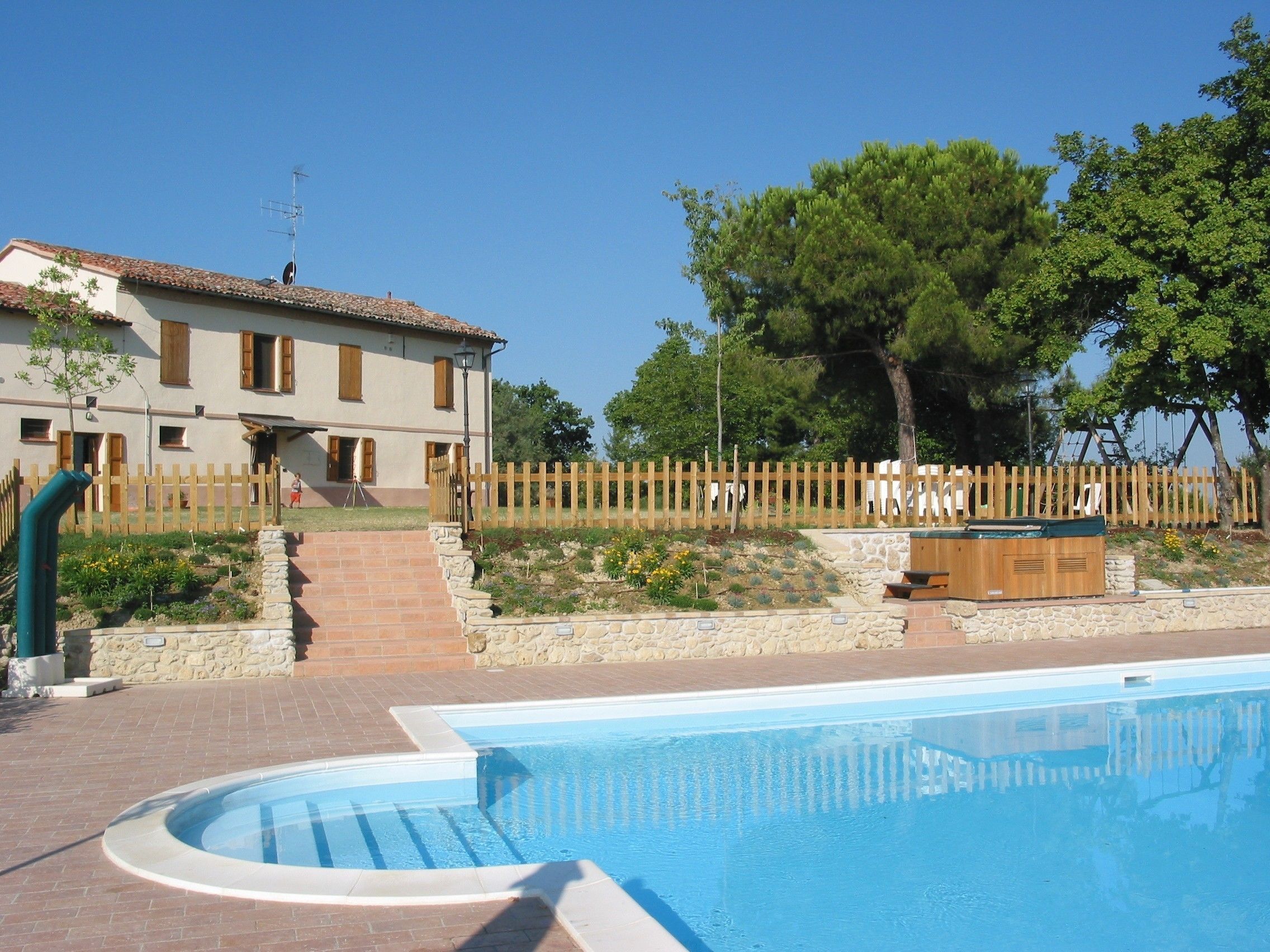 Une piscine bordée de pierres, une terrasse en bois et un mur en pierre.