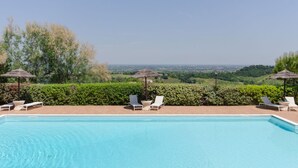 Una piscina con sillones de descanso y sombrillas, rodeada de follaje y vistas al paisaje.