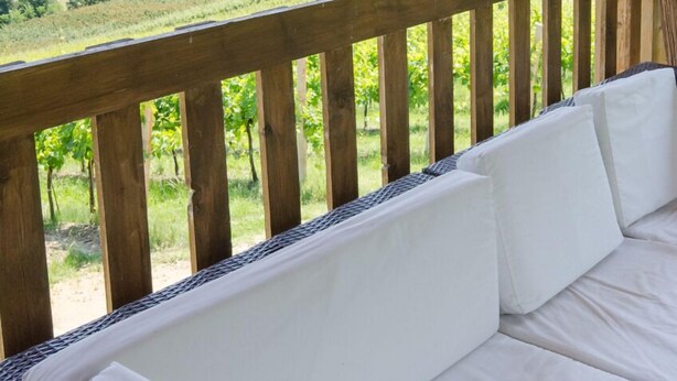 Una terraza de madera con un sofá blanco que da a onduladas colinas verdes.
