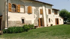 Un edificio de dos pisos con fachada de piedra y estuco, numerosas ventanas de madera y un césped bien cuidado.