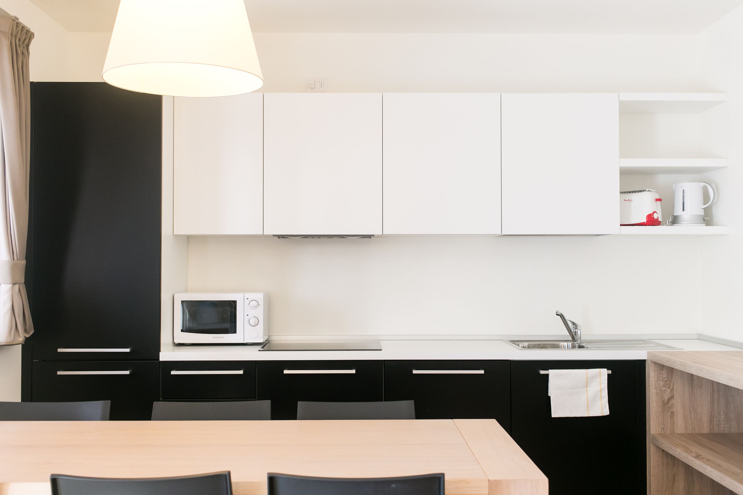 Une cuisine moderne avec des meubles blancs, un four à micro-ondes, un évier et une table à manger en bois, accompagnée de chaises.
