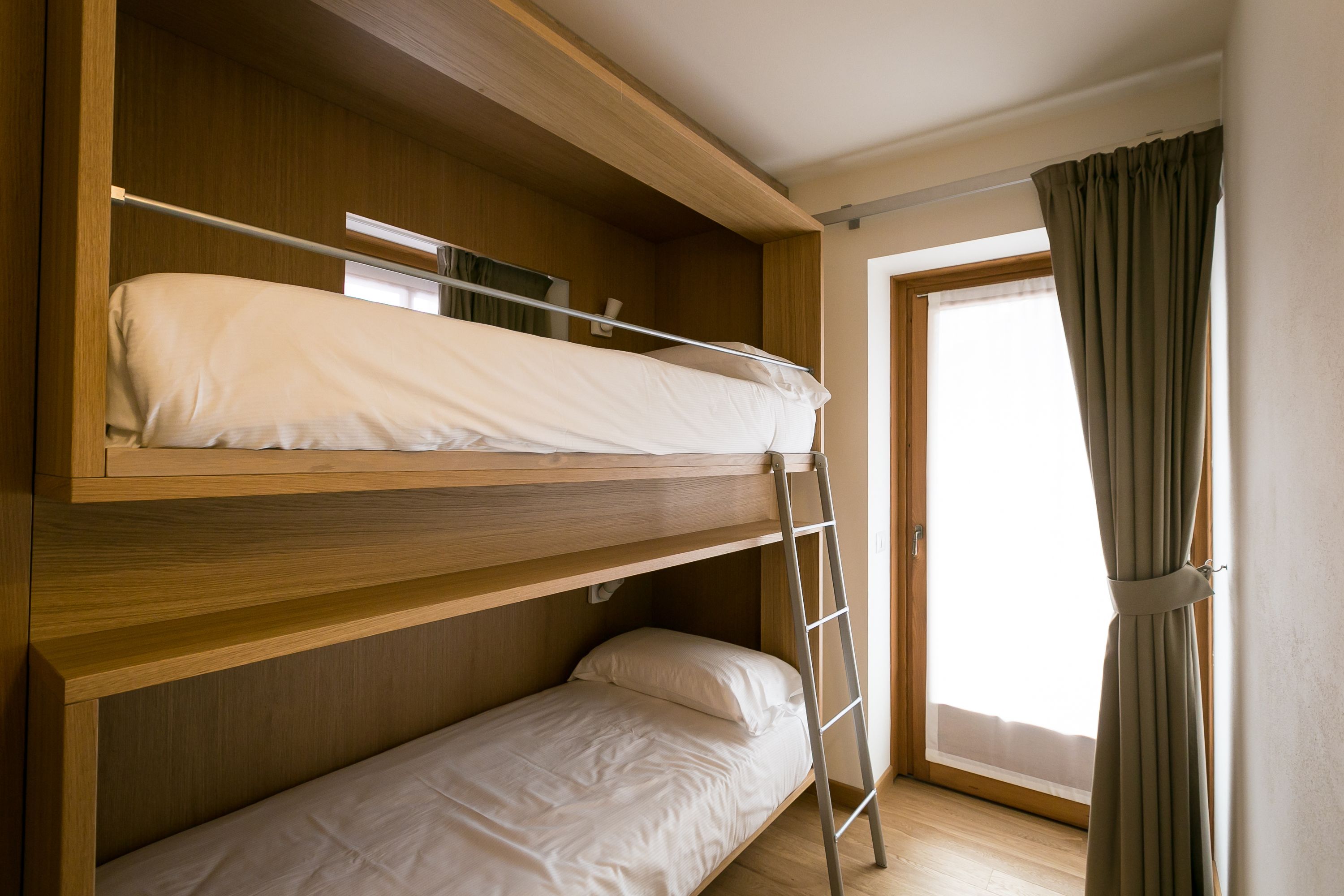 A bunk bed room with a wooden headboard, a ladder, and a window with curtains.