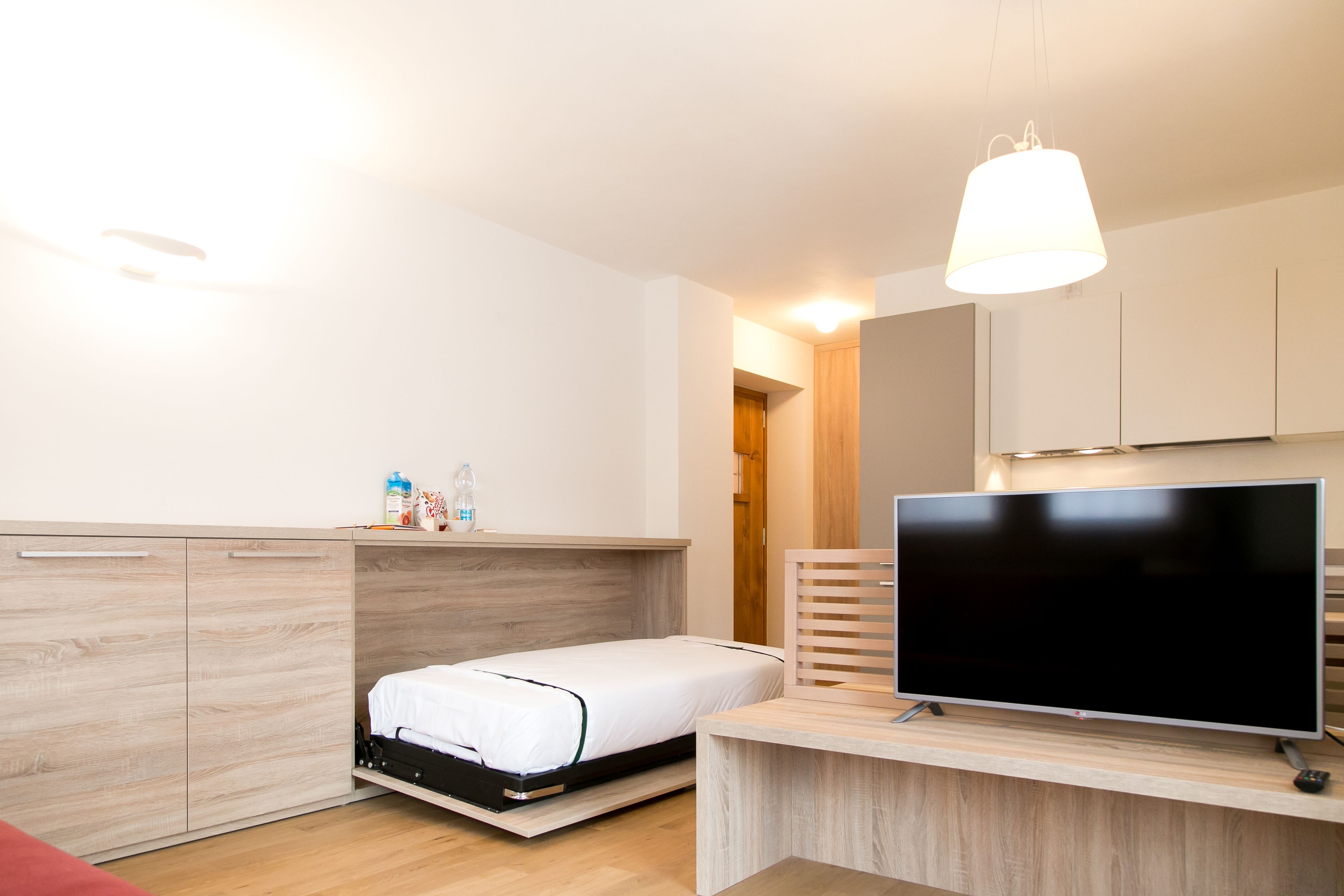 A compact bedroom with a bed, a TV, and a desk.
