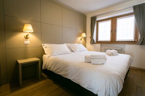 Habitación de hotel con una cama grande, dos lámparas de noche, una mesita de noche pequeña y una ventana con cortinas.