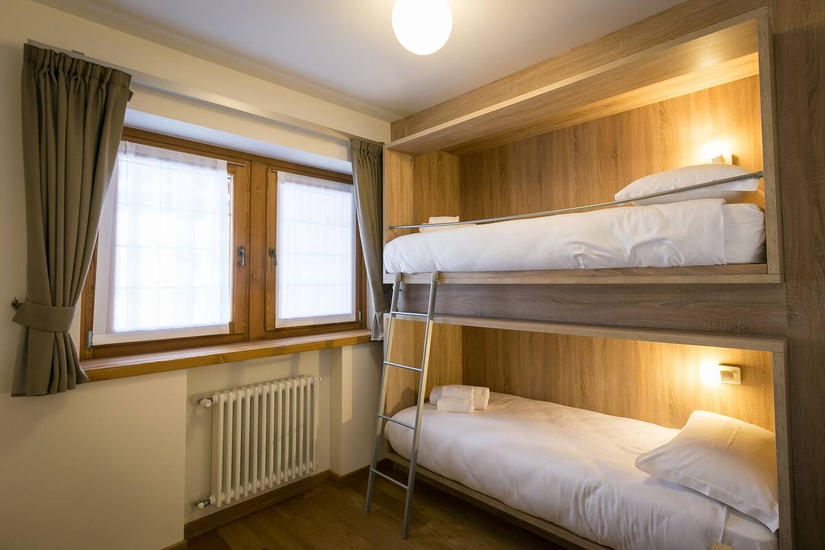 Et soveværelse med køjeseng, stige, et vindue med gardiner og en radiator.