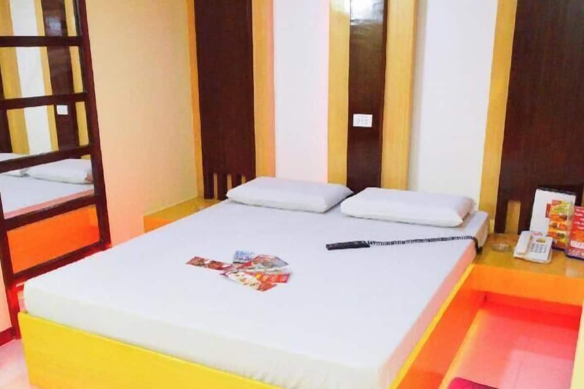 A hotel room with a bed, a bedside table with a phone and a magazine, and a mirror on the wall.