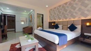 A modern hotel room with a large bed, a desk, and a chair. There is a bathroom visible through a glass door.