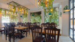 A restaurant with wooden tables and chairs, hanging plants, and pendant lights.