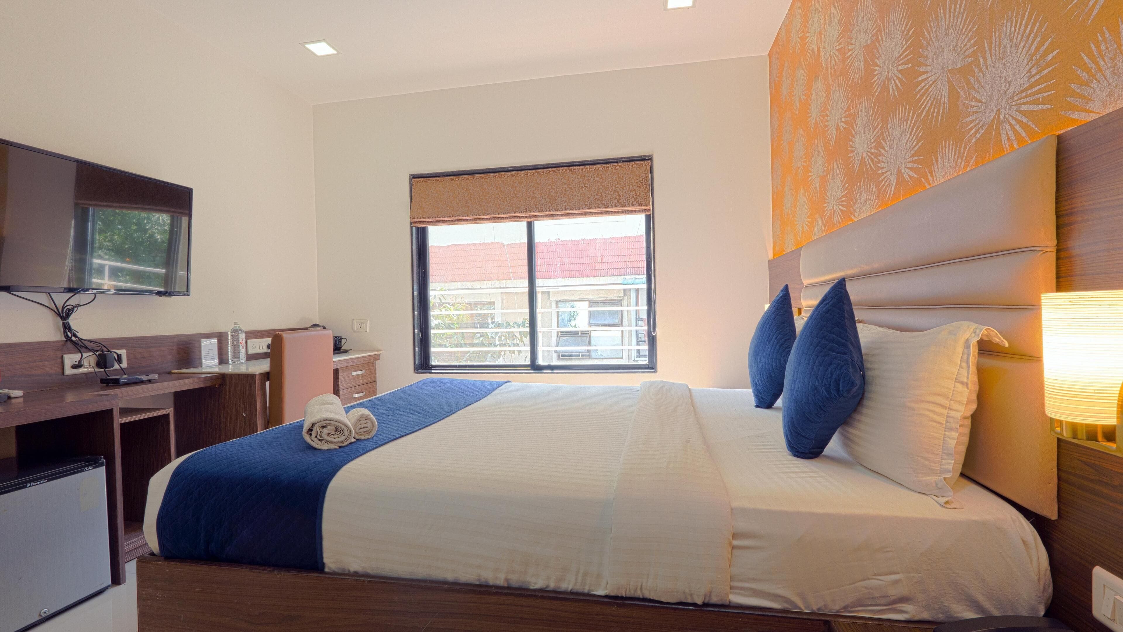 A hotel room with a bed, a desk, a television, and a window with a view of buildings.