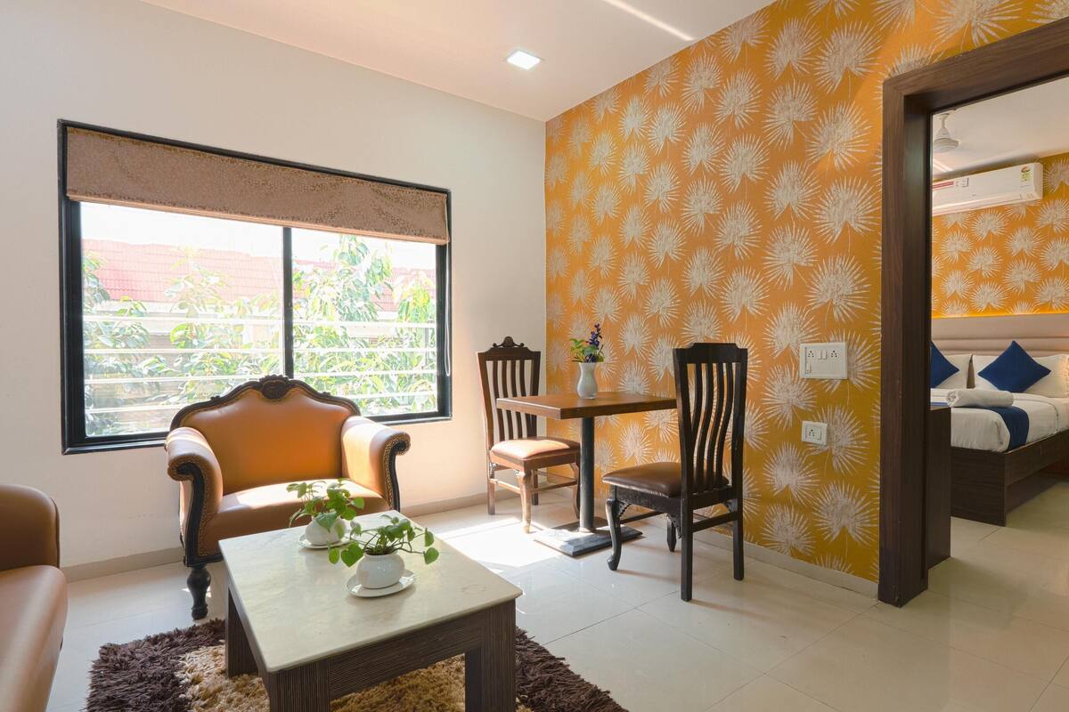 A hotel room with a dining area, a bed with a headboard, and a view of the outside.