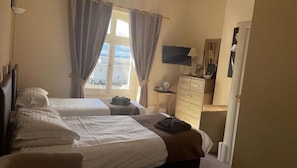 Habitación de hotel con dos camas, un escritorio con silla, televisor y ventana con cortinas.