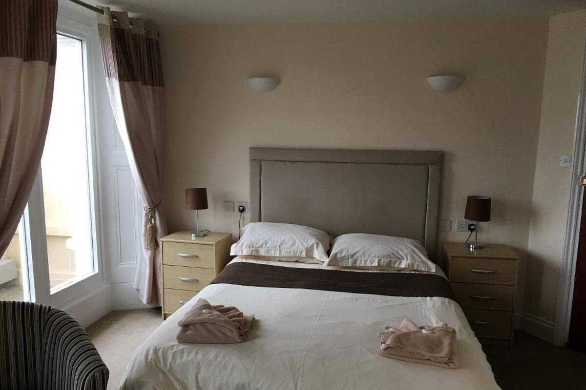 Una habitación de hotel con una cama, dos mesitas de noche, una silla y una ventana con cortinas.