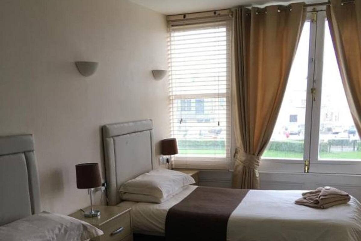 Habitación de hotel con dos camas, ventana con cortinas y vistas al exterior.