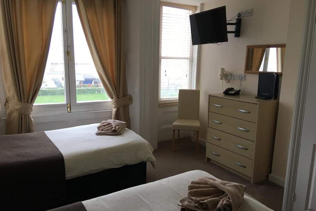 Habitación de hotel con dos camas, un escritorio, una cómoda, televisión y ventana con cortinas.