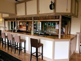 A bar area with a long counter, multiple stools, and a variety of bottles and glasses.