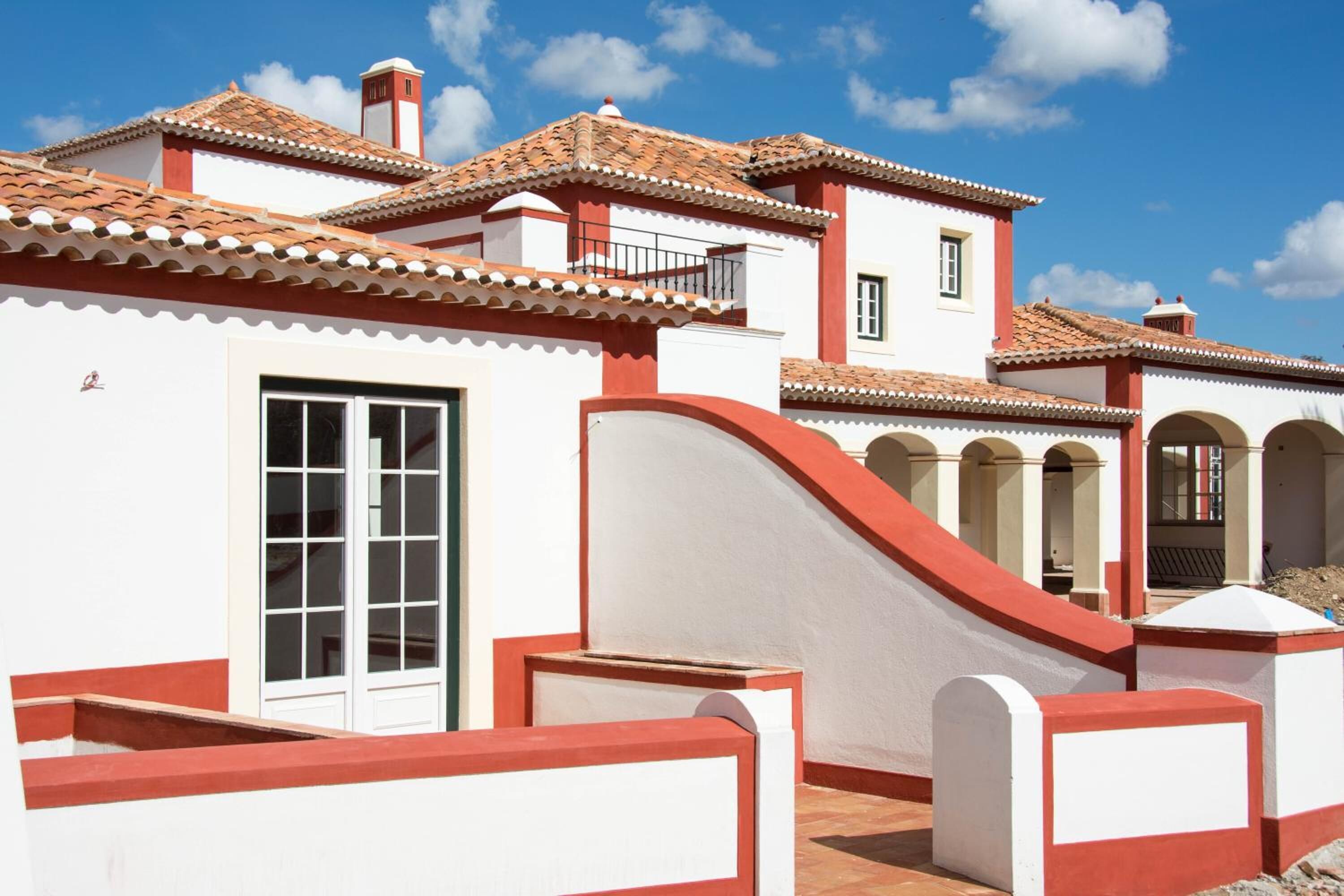 Un edificio blanco con detalles rojos, techo de tejas y una escalera que lleva a un nivel superior.