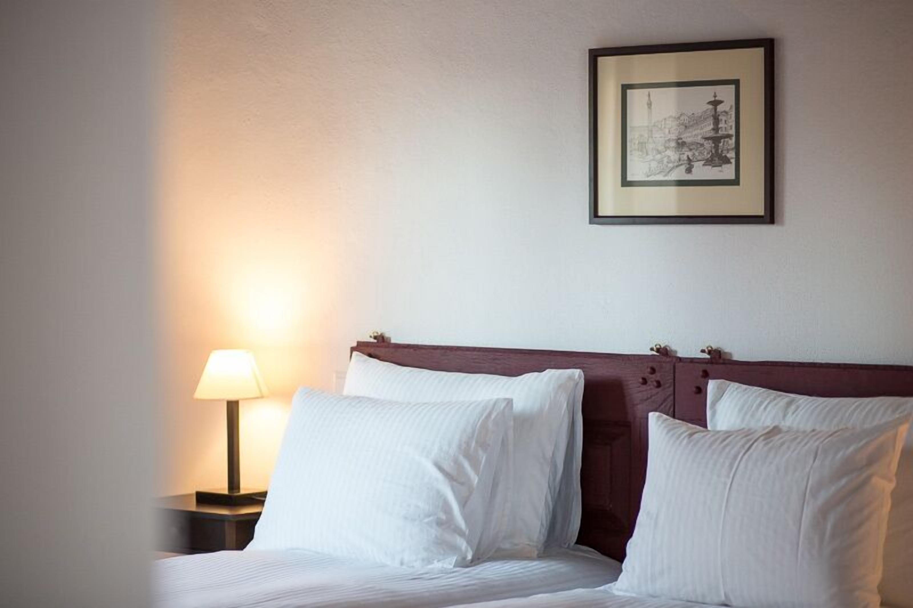 Een hotelkamer met een bed, een nachtkastje met een lamp en een lijst aan de muur.
