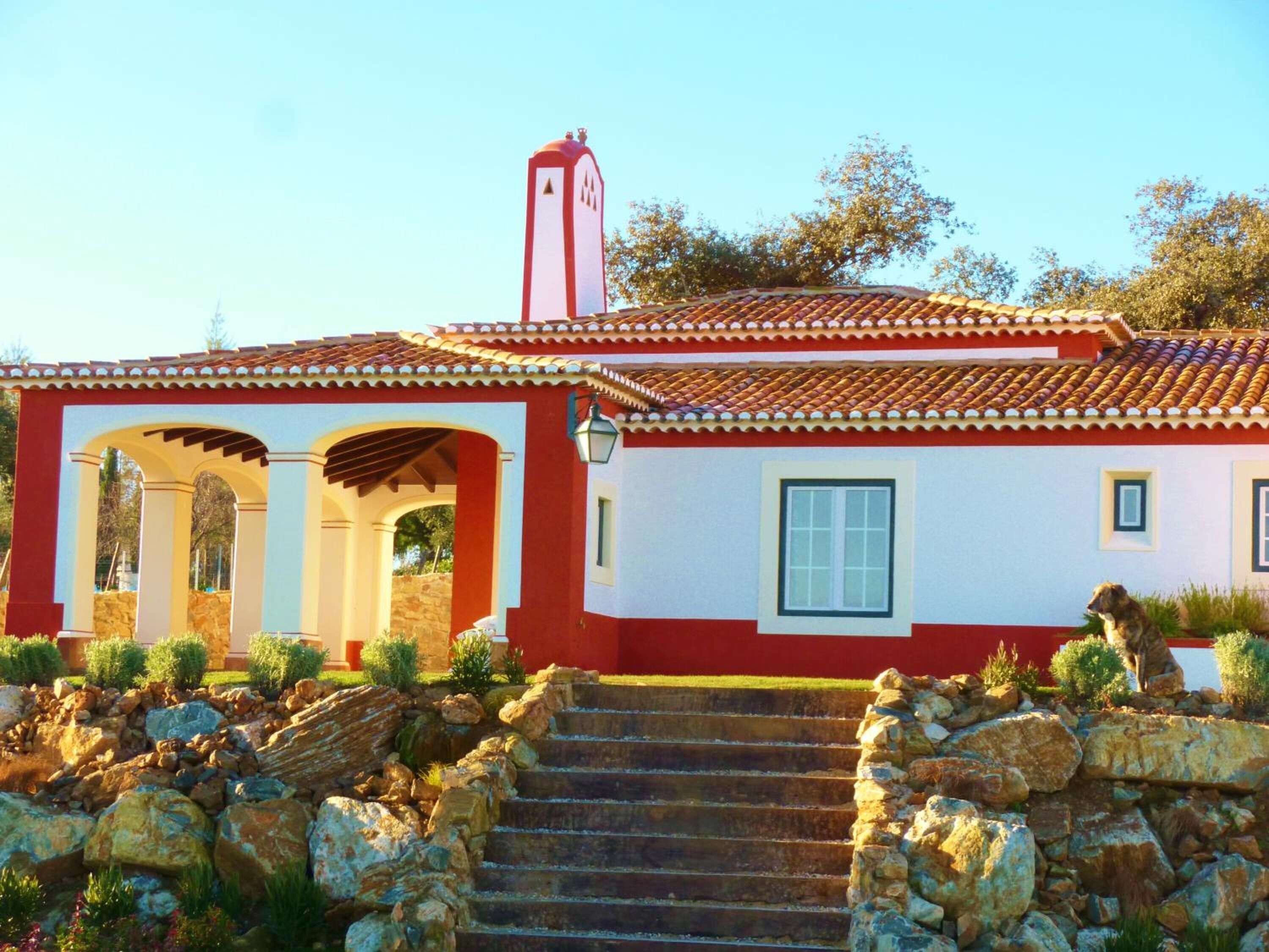 A traditional house with a red and white facade, a stone staircase leading to the entrance, and a stone wall surrounding the property.