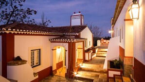 Un patio con techo de tejas, escalones de piedra y un edificio blanco con detalles rojos.