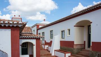 Un patio con una escalera que lleva a una puerta, rodeado de edificios con paredes rojas y blancas y tejados de tejas.