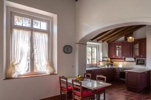 Una cocina con armarios de madera, una mesa de comedor con sillas y una ventana con cortinas.
