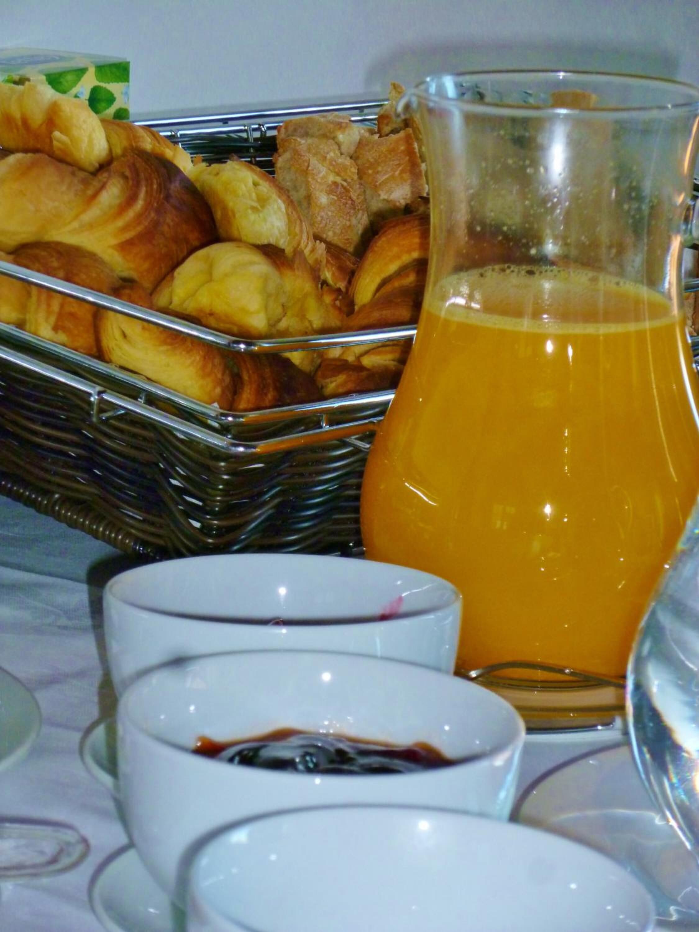 Ein Frühstückstisch mit Gebäck, einem Saftkrug und kleinen Tassen mit Kaffee oder Tee.