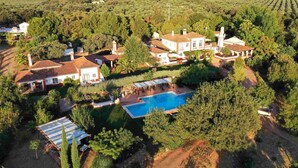 Vista aérea de una propiedad con varias edificaciones, piscina y abundante vegetación.