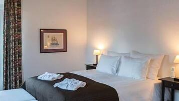 Une chambre d’hôtel avec un grand lit, deux tables de chevet, une commode, un tableau encadré au mur et une fenêtre avec des rideaux.
