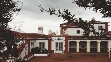 A two-story building with a red-tiled roof, white walls, and a central entrance.