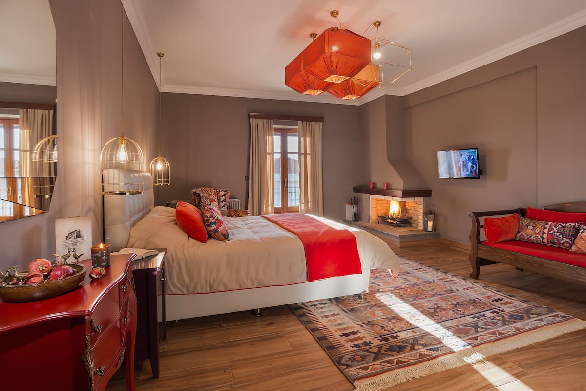 Ein Schlafzimmer mit einem großen Bett, einem roten Sofa, einem Kamin und einem Fernseher an der Wand.