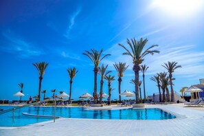 A swimming pool with palm trees and lounge chairs, surrounded by umbrellas and a clear blue sky. - Aljazira Beach & Spa  -  Families and Couples Only (Mezraia)