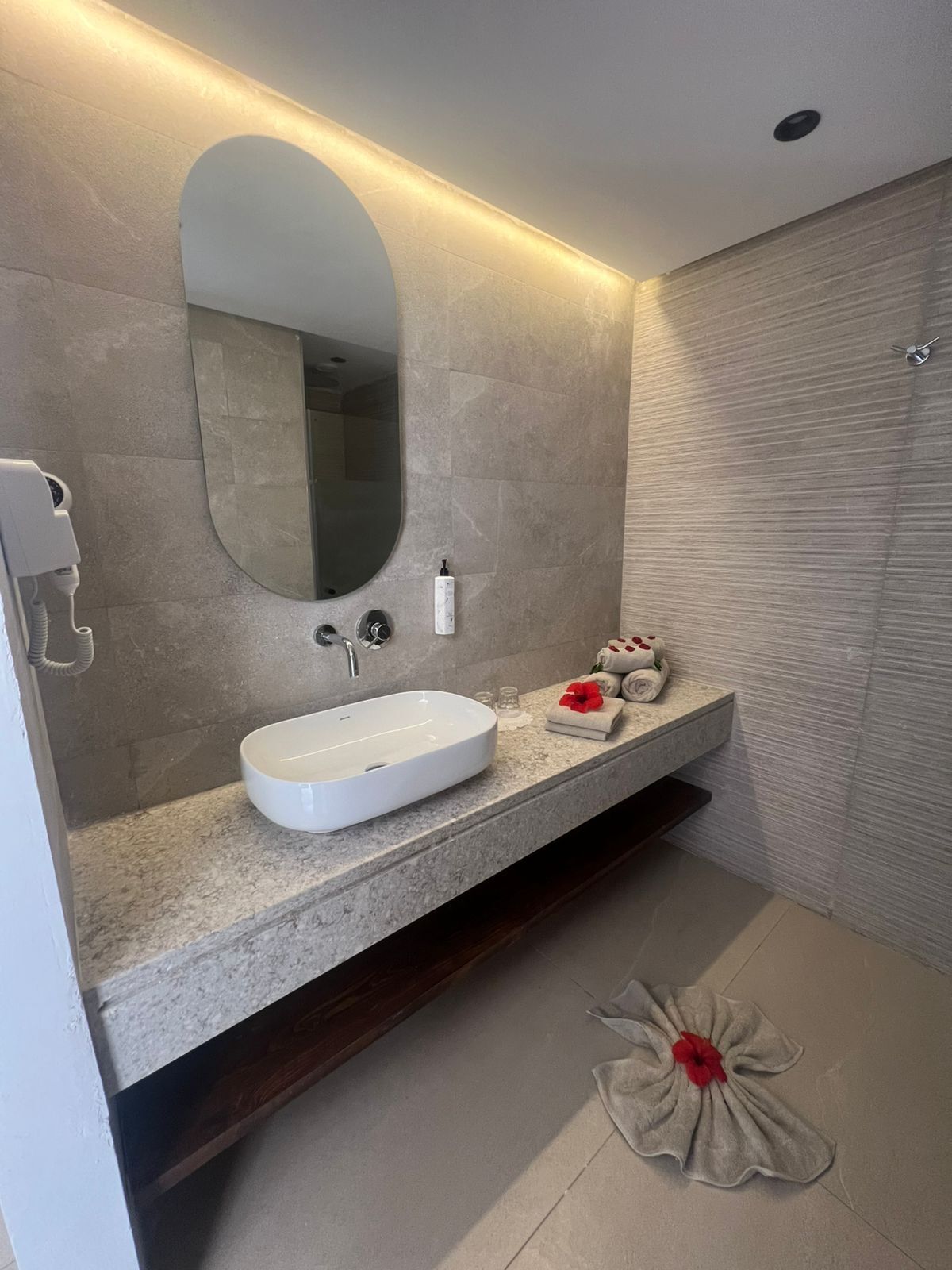 A modern bathroom with a large oval mirror, a white sink, and a towel rack.