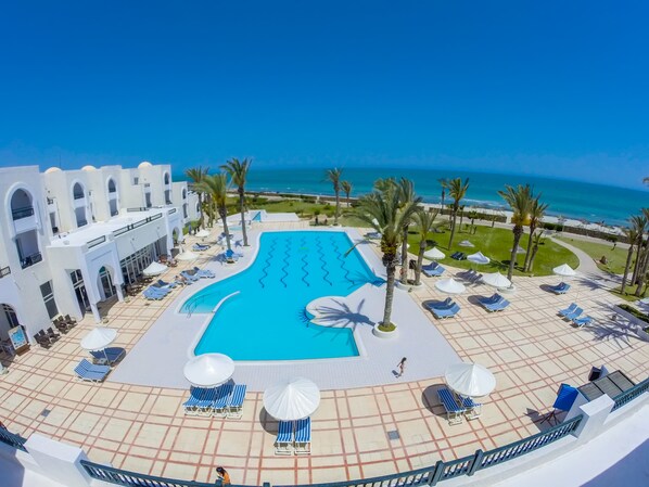 A resort pool area with a clear view of the ocean, lounge chairs, umbrellas, and a white building with arches. - Aljazira Beach & Spa  -  Families and Couples Only (Mezraia)