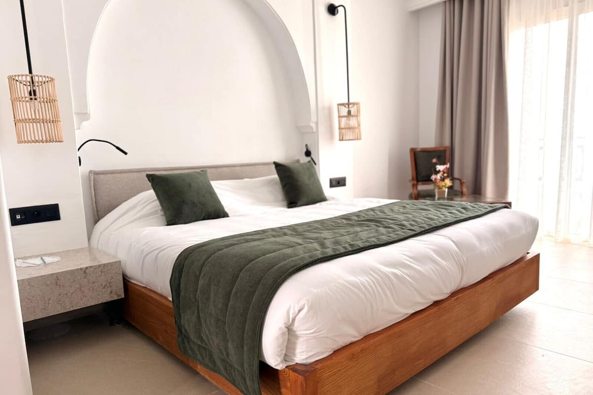 Ein modernes Hotelzimmer mit einem hölzernen Bett, weißer Bettwäsche und einer grünen Tagesdecke.