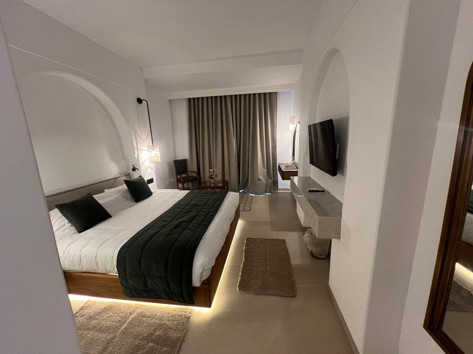 Habitación de hotel moderna con una cama grande, televisión, escritorio y baño al fondo.
