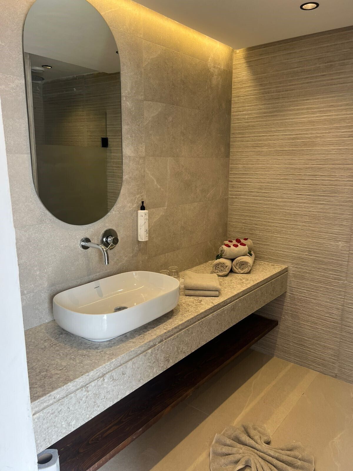 A modern bathroom with a large oval sink, a mirror, and a towel rack with neatly folded towels.
